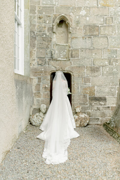Fine art wedding photography of a Bride entering the church through a historic entrance on her private estate wedding day in Scotland, planned by one of the UK's best wedding planners, Laura McCranor Events. The wedding venue was Blairquhan estate. Image by multi-award winning luxury wedding photographer uk, Jill Cherry Porter.
