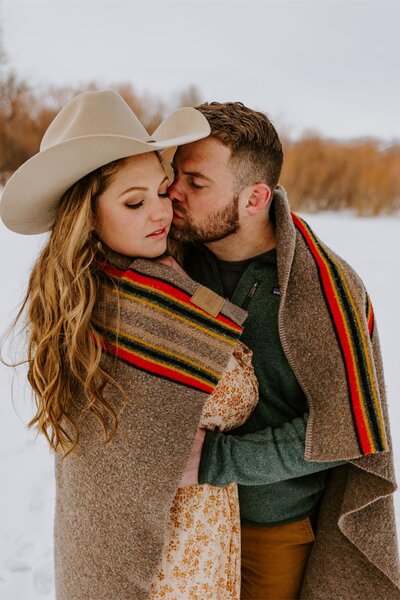 Man kisses his significant other while wrapped in a blanket.