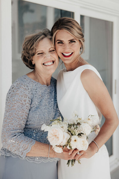 Elegant bride and mother of bride with big smiles holding on to bouquet