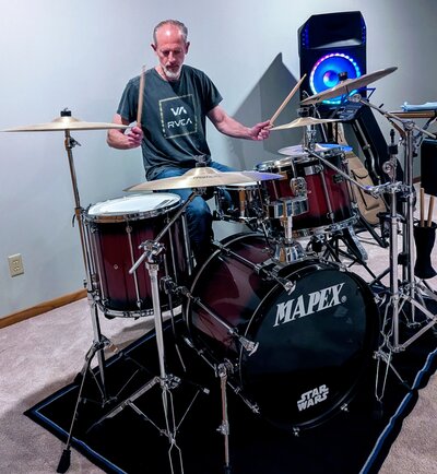 Before photo of man playing drums in dimly lit room, captured before professional dating profile photography session