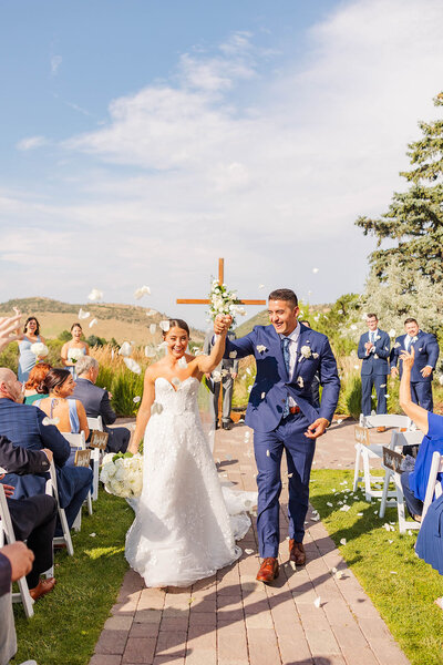 Bride and groom walking down the aisle after their first kiss at The Manor House in Littleton, Colorado, surrounded by cheers and love from their guests.