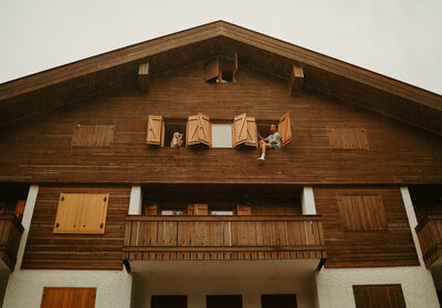 A couple sits in the window of an A-frame cabin in the Dolomites
