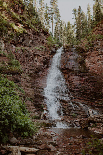 Bride and groom stand in front of a waterfall at Dunton Hot Springs