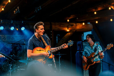 Red Clay Strays Lead singer playing guitar during a live concert with stage lighting and bandmates in the background, captured by Joseph Mayden as part of his professional event coverage.