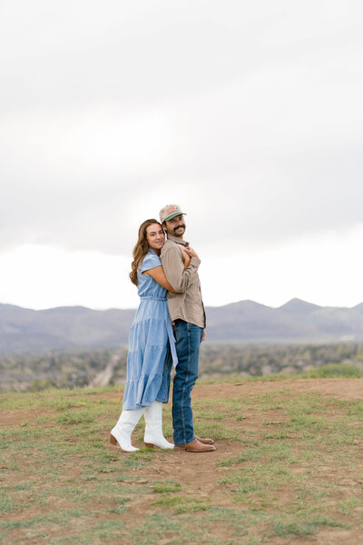 Woman hugging fiancé from behind, smiling at camera