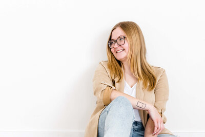 headshot of blonde business owner smiling to the side with glasses. wearing tan blazer and jeans