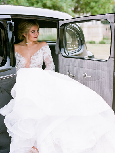 Bride stepping out of classic vintage car in ballgown