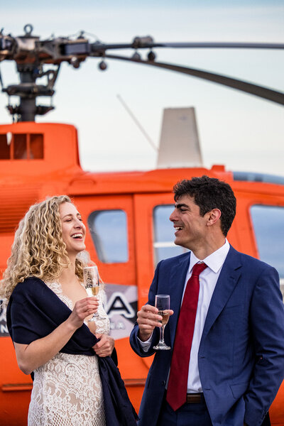 Couple sharing a champagne toast with helicopter in background.