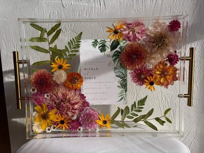 An acrylic tray with pressed flowers representing a bridal bouquet preservation service offered by Dame Designs.