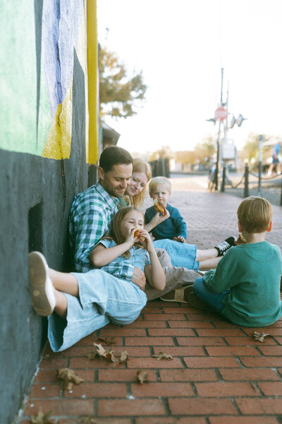 A family sitting on the sidewalk in front of a mural in downtown Marietta, GA. 