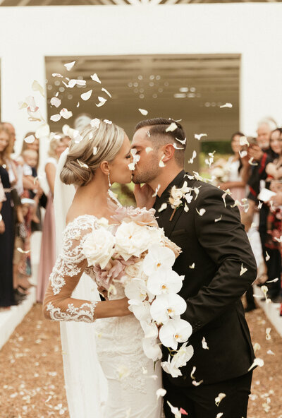 Newlyweds embrace in a kiss, surrounded by falling confetti bliss.