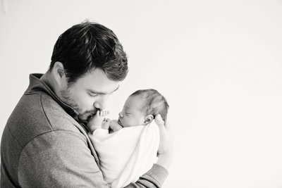 dad kissing baby toes with baby in ivory swaddle