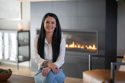 woman with long dark hair smiling in front of a fireplace