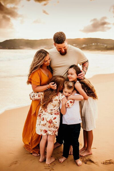 Family dressed in warm colors hugging near a beautiful beach