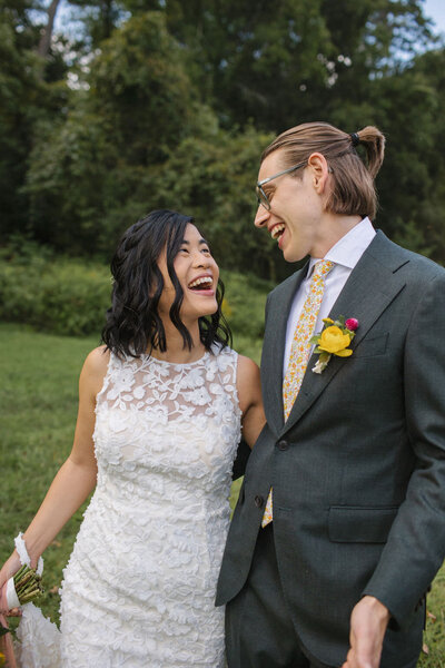 Catskills wedding couple look into each others' eyes as they laugh. Bride in lace dress, groom in gray suit with floral tie and yellow flower boutonniere.