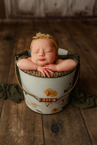 baby girl with a pouty lip sleeping in a floral bucket newborn photoshoot
