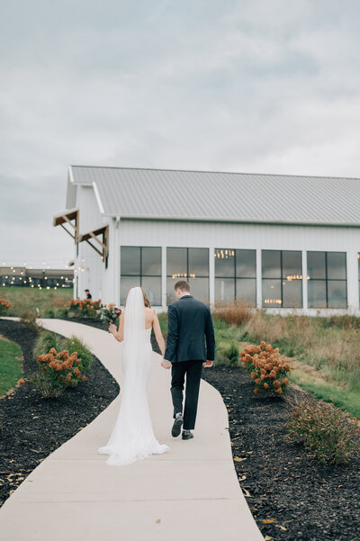 Bride and Groom walk back to their wedding venue. Bride’s dress is covered in pearl accents, and groom is wearing a navy blue and black tux. Photo by Anna Brace, who specializes in wedding photography in Omaha.