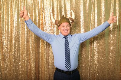 Man in photobooth with gold sparkle background, wearing a Viking hat