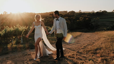 Modern bride and groom walking through a vineyard at sunset.