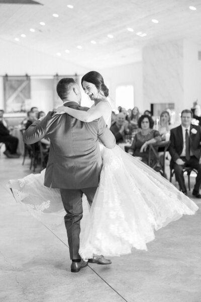 Bride smiling while groom lifts her on dance floor