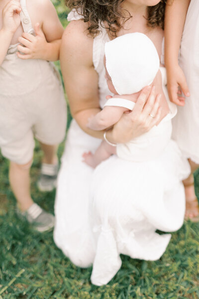 Mother holds newborn baby with dad  and daughter standing by playing at Newborn Photography Alexandria session.