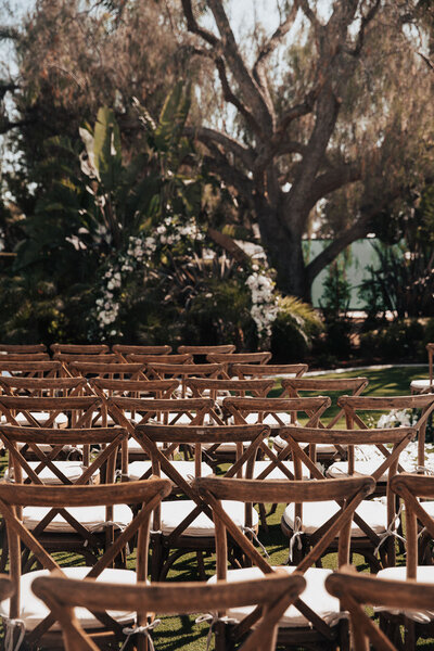 Several rows of wooden chair back-rest lining  up  in front of a decorated wedding arbor