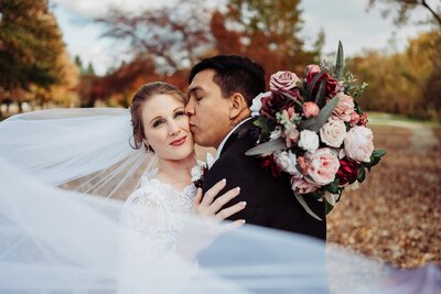 Romantic Veil shot. Bride looking off while groom kissing her temple. Veil swooped in front. 