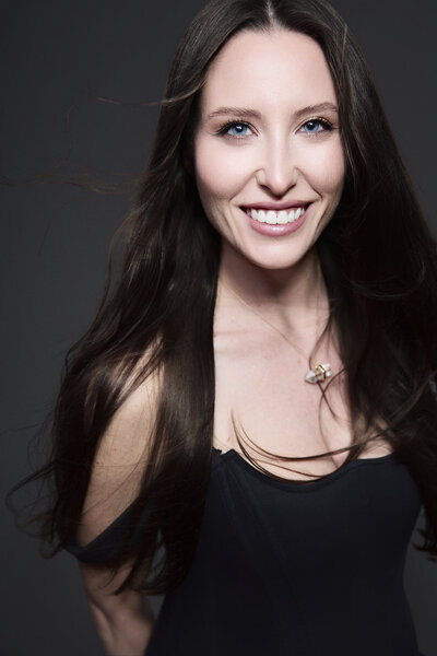 Color portrait of fashion photographer smiling against dark background