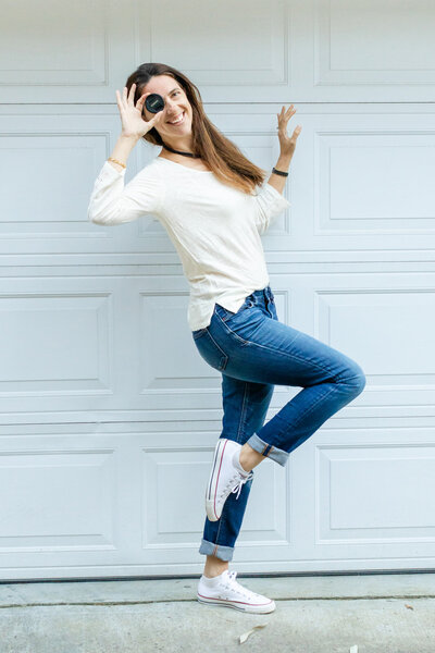 woman in casual outfit jeans and white top standing playing with a camera cap in pockets