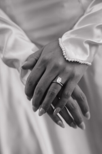A close-up black and white image of a bride’s hands gently resting, her ring on full display.