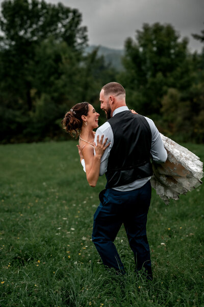 Couple spins in a green field of tall grass as they laugh together after they get married.