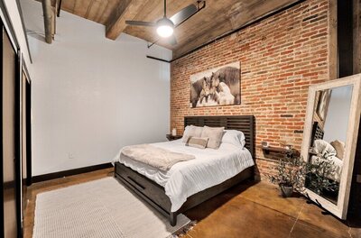 Bedroom with King bed and exposed brick in this three-bedroom, two-bathroom industrial modern loft condo in the historic Behrens building in downtown Waco, TX.