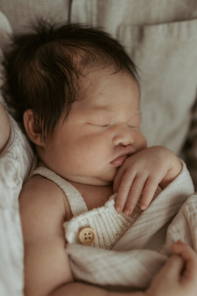 Sleeping newborn baby dressed in neutrals during her first in-home newborn photoshoot with her mum and dad.