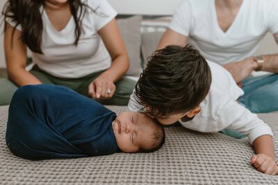 Toddler brother kissing newborn baby during in home session.