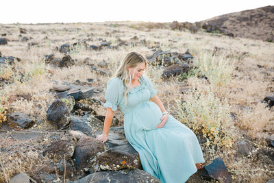 mom sitting on black rock and holding her belly for maternity photos