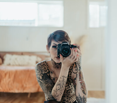 Woman with short hair and tattoos holds camera up to face.