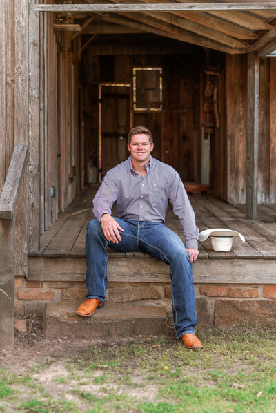 Tarleton State graduate posing in jeans and boots sitting on a porch during senior session in Stephenville, Texas.
