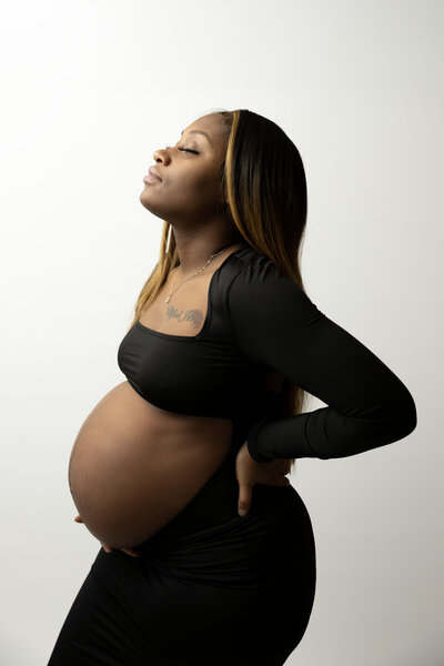 An expecting mom holds her belly that sticks out of a tight black dress.