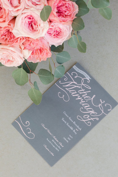 Pink peonies frame a gray and pink wedding program