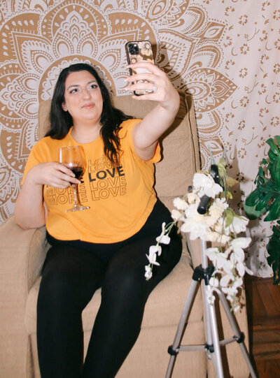 Sarah Weiss in an orange t-shirt, taking a selfie for her Tiktok and Instagram marketing