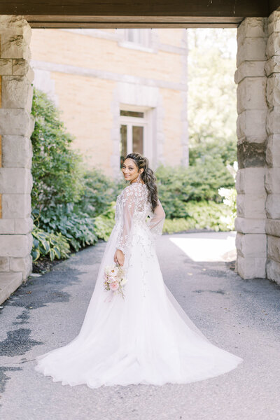 Bride stands under stone arch at the Great Marsh Estate in Virginai