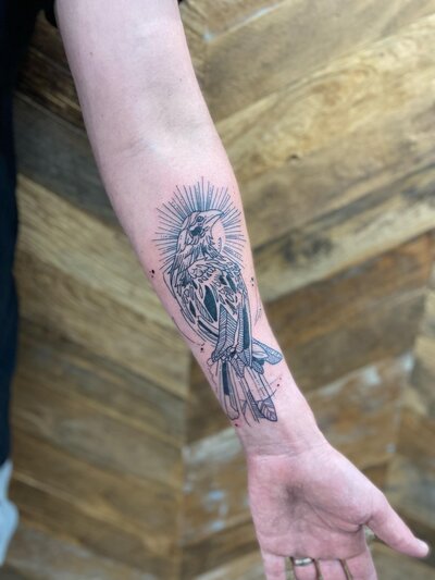 Black and white tattoo of bird on fore arm