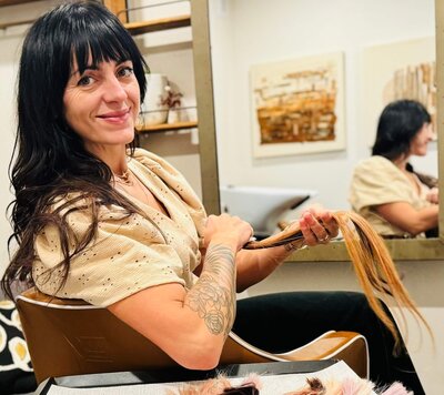 Hair stylist sits in her salon chair holding sample hair extensions.