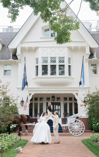 A groom twirls his bride in front of a manor with a horse and carriage at their wedding on Mackinac Island