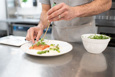 A chef putting the final touches a plate of salmon.