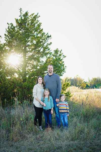 A family of four stands in front of a tree at sunset at John Saxon Park in Norman.