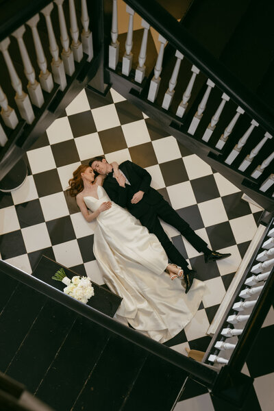 bride and groom laying on black and white tiled floor look at each other