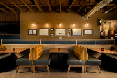 Warm restaurant interior featuring mustard and teal banquettes with wooden tables - signature hospitality interior design services near me.