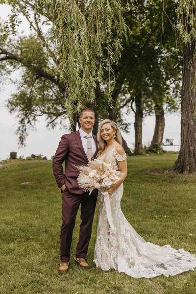 Bride and Groom in Fon du Lac Wisconsin . Bride looking at the camera holding her bouquet under a tree at their private estate wedding by milwaukee wedding planner.