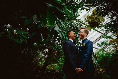 A couple looking at each other and holding hands in a botanical garden.